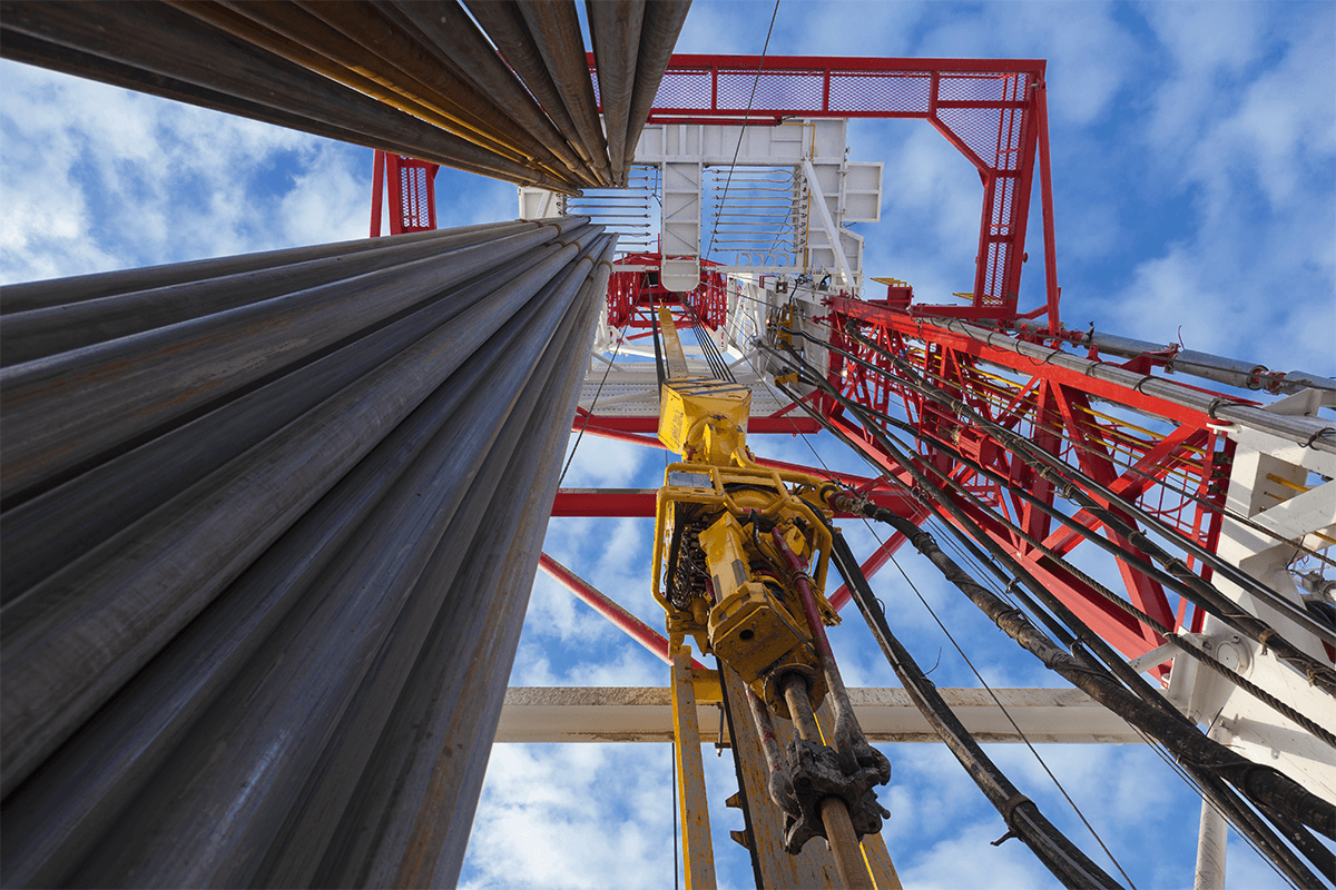 supplychain Marmon Keystone Low-angle view looking up at an oil drilling rig against a blue sky with clouds, featuring metal pipes supplied by a leading distributor, machinery, and red-and-white structural components essential to the supply chain.