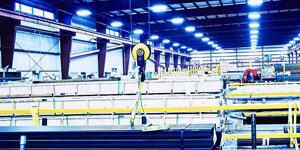 iso-img-29 Marmon Keystone A brightly lit industrial warehouse interior with stacked tube pipes and metals, yellow safety railings, and a hoist system hanging from the ceiling, showcasing a busy supplychain distributor environment.