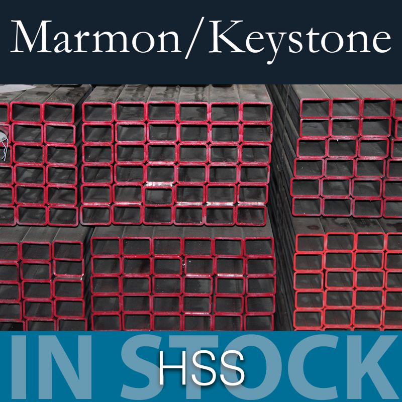 post-1-7 Marmon Keystone Stacks of rectangular hollow structural steel sections with red-painted edges are arranged in rows. The text above reads "Marmon/Keystone" and below reads "IN STOCK HSS metals distributor".
